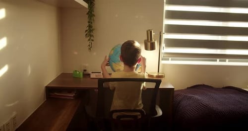Young Boy Studying a Globe at Desk
