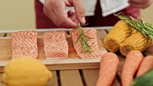 Seasoning salmon with rosemary on a cutting board