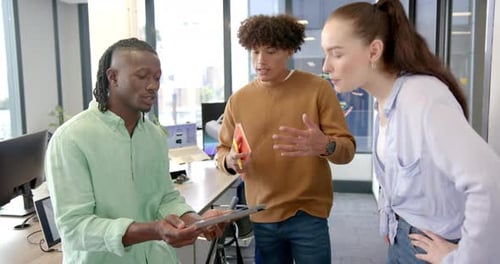 Discussing project details, diverse team collaborating using tablet in modern office