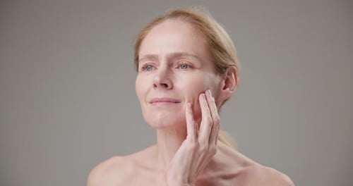 Mature Woman Gently Touching Face in Studio Setting