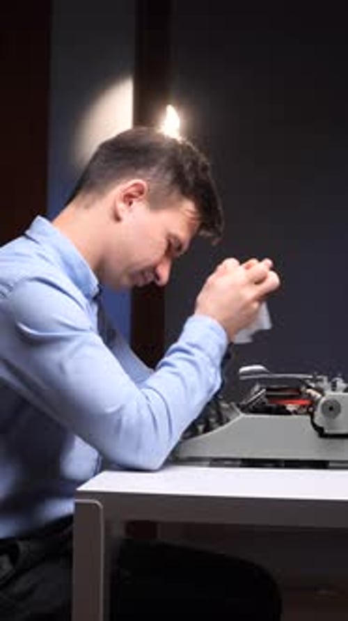 Frustrated Man with Typewriter Holds Head in Hands