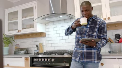 Man Drinking Coffee Using Tablet in Modern Kitchen