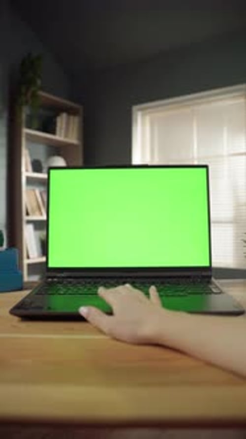 Woman's Hand Interacting with a Laptop Featuring a Blank Green Screen Display on a Wooden Desk
