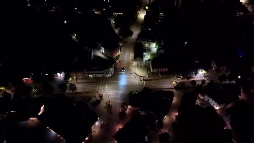 Aerial top down shot of vehicle on junction turning into street of small american town. Clear night