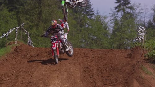 Motocross Riders Jumping Over Hill on Dirt Track