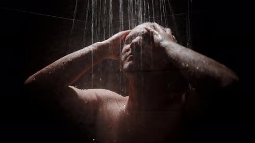 Un homme prend plaisir à prendre une douche rafraîchissante dans une salle de bain sombre avec de l'eau qui coule