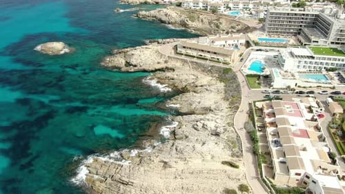 Aerial reveal view of a beautiful sea and rocky beach with resorts and natural parks in the backgrou