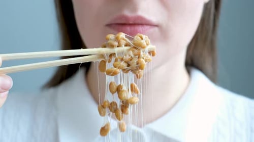Young woman using wooden chopsticks eating Japanese natto beans front view close-up.