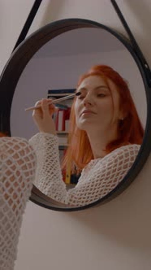 Woman applying eyeshadow in mirror at home