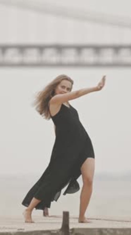 A Woman in Black Dress Dancing on the Pier in