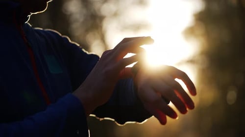 Silhouette of a Runner Checking a Smartwatch on the Wrist During an Early Morning Park Run Sunlight