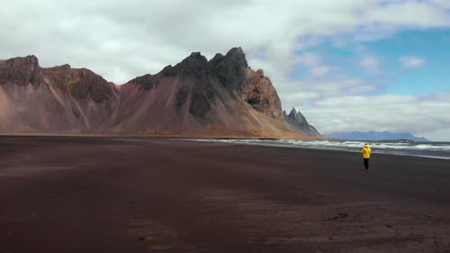 Man in a Yellow Jacket Walks Along the Black Sand Beach of Stokksnes in Iceland