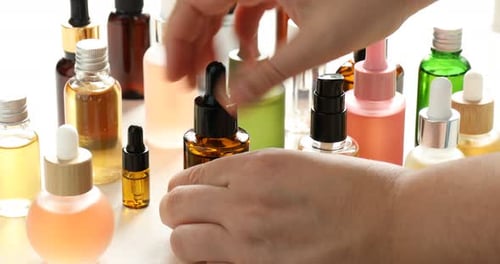 Woman dripping cosmetic product into bottle at white table, closeup