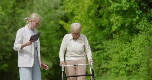Woman Helps Senior with Walker in Green Space