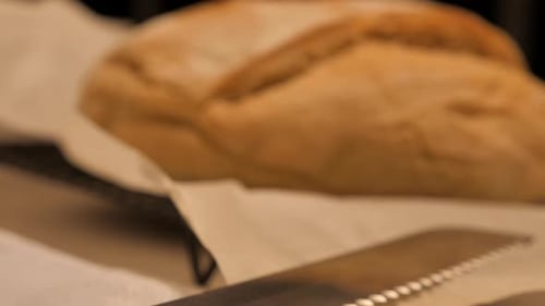 Slow pan over serrated knife towards freshly baked loaf of sour dough bread topped with flour sittin