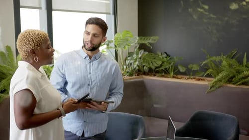 Smiling diverse colleagues holding tablets in modern office with indoor plants, copy space
