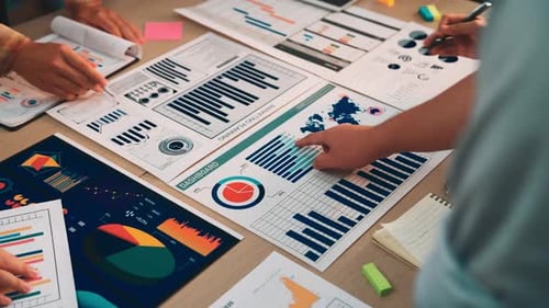 Diverse team analyzing data charts and graphs on office desk with digital devices and notebooks for