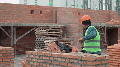 Bauarbeiter baut Backsteinmauer auf der Baustelle Arbeiter verlegt Ziegel und verteilt Zement darauf