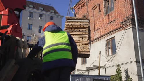 Crane Lifts Wooden Pallets Under Careful Watch of Worker