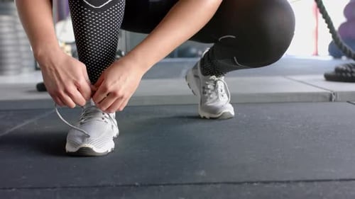 Tying shoelaces, woman preparing for workout in gym, wearing athletic shoes