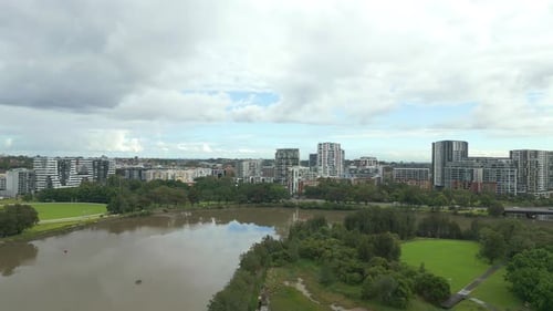 Luftaufnahme eines wunderschönen Parks und Flusses mit Gebäuden im Hintergrund an einem bewölkten Tag