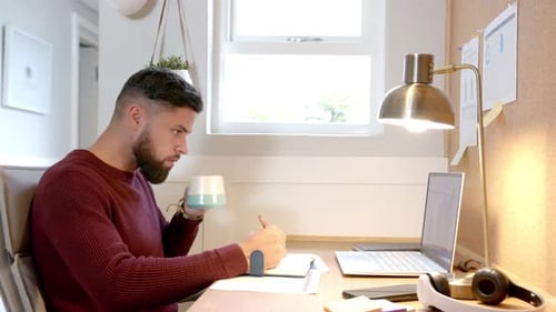 Von zu Hause aus arbeiten, Mann trinkt Kaffee und benutzt Laptop am Schreibtisch