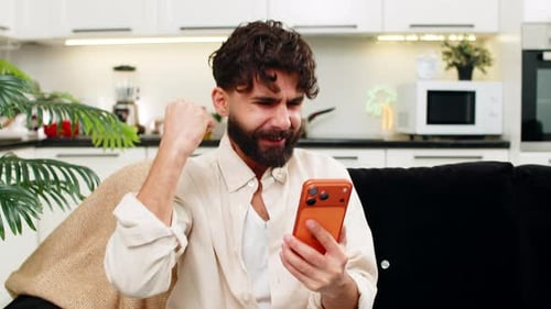 Man Cheers While Looking at Phone on Couch