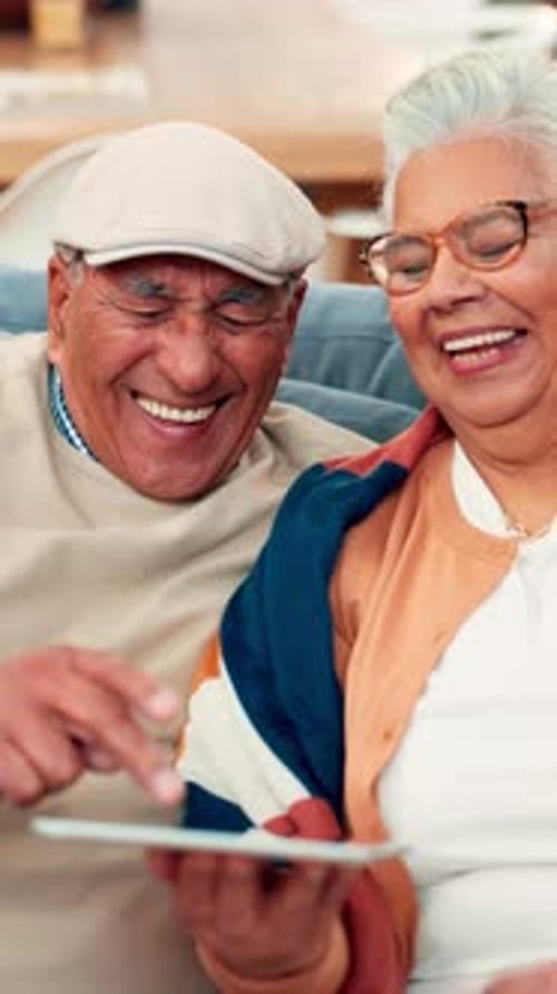 Senior Couple Laughing While Using Tablet Indoors