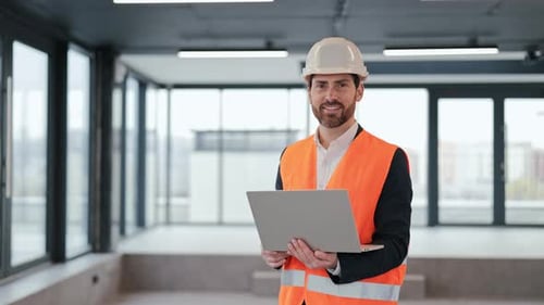 Confident Engineer Smiles with Laptop in Modern Office Building