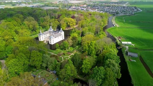 Aerial view of a historic castle surrounded by a forest, with vast green fields, winding waterways