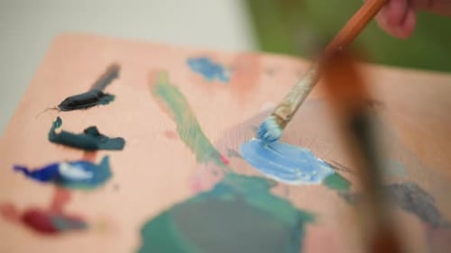 Artist Mixing Blue and White Paint on Palette with Brush