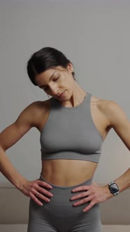 Athletic Woman Stretching Neck in Gray Sportswear Indoors