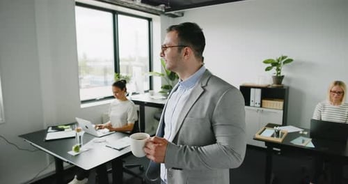 Office Workers At Desks With Man Drinking Coffee