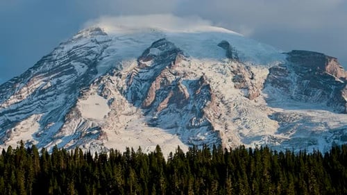 Majestic view of Mount Rainier rising above a dense evergreen forest under a moody sky, captured in