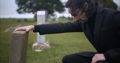 Sad, emotional man in cemetery grieving over death of loved one.