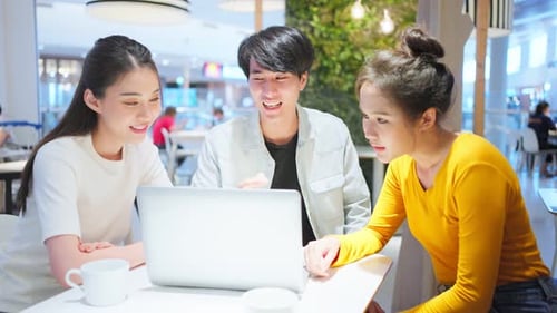 Group of Asian friends talking and using laptop computer in restaurant.