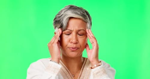 Headache, stress or mature woman on green screen with anxiety, temple massage or burnout in studio