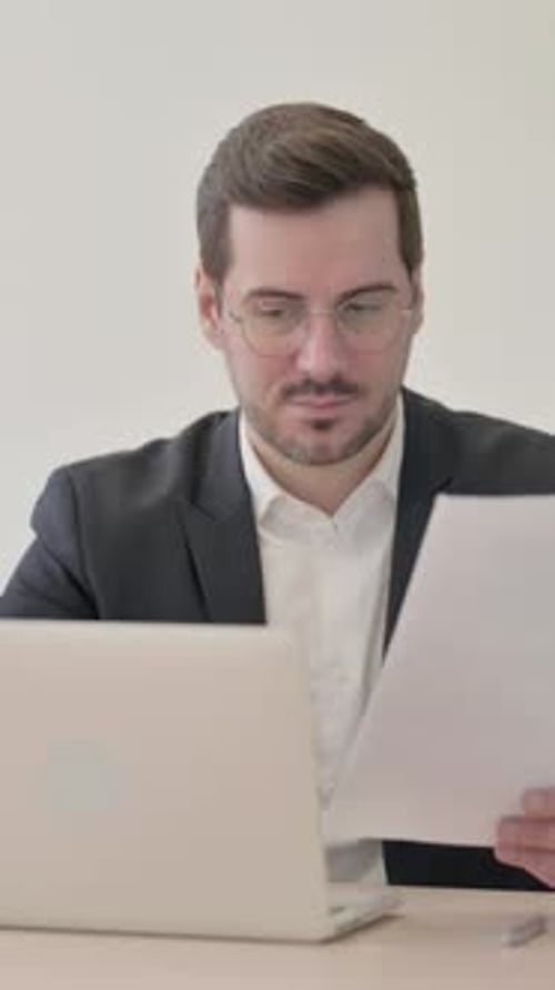 Excited Man Reading Documents at Work With Laptop