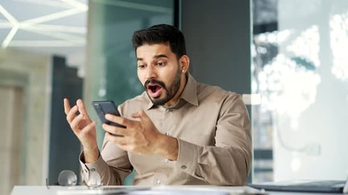Man Reacts to News on Smartphone in Office