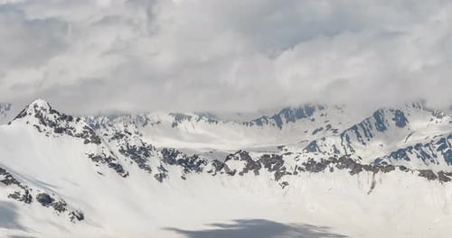Air flight through mountain clouds over beautiful snow-capped peaks of mountains and glaciers.