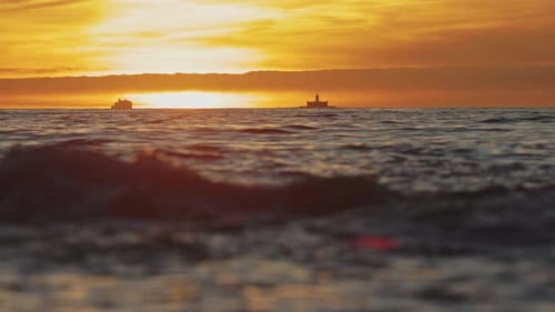 Dark Sea Waves Under an Orange Bright Sunset Ships in the Distance
