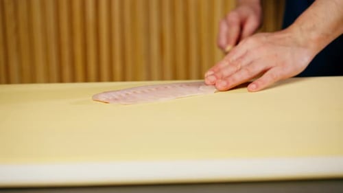 Close Up in a Japanese Restaurant Chef in a Blue Uniform Cuts Fish for Sushi Into Slices on a Yellow