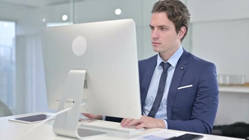 Focused Young Businessman Working on Desktop in Office