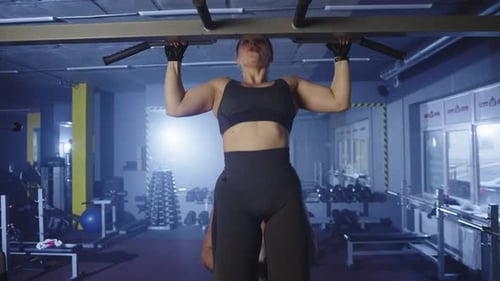 A Young Sporty Girl is Doing Pullups on the Exercise Machine in the Gym