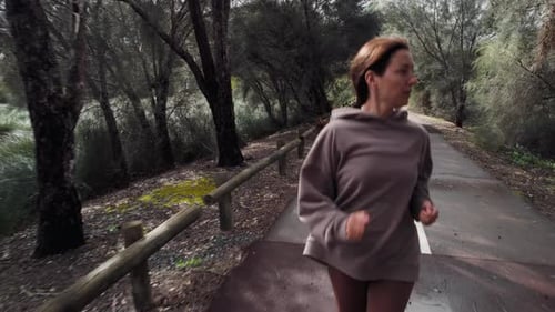 A woman jogs along a forested trail during early morning, surrounded by trees