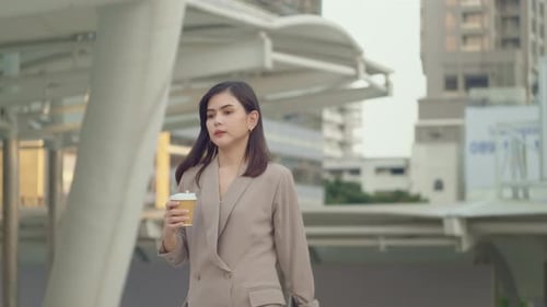 A young beautiful businesswoman is drinking coffee walking in Modern city
