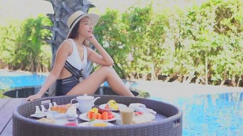 Young woman chilling by pool with tray of treat, coffee, snack