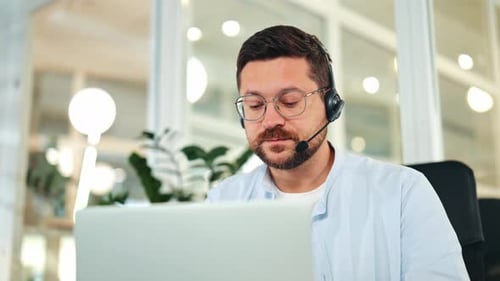Concentrated Male Specialist Working on Laptop with Headset in Office