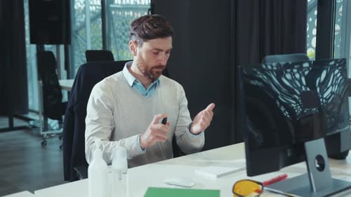 Man Uses Hand Sanitizer at Office Desk