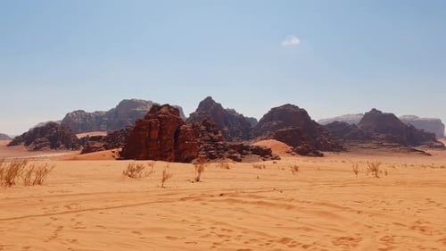 Pan across golden sand with sparse shrubbery, typical Wadi Rum vista